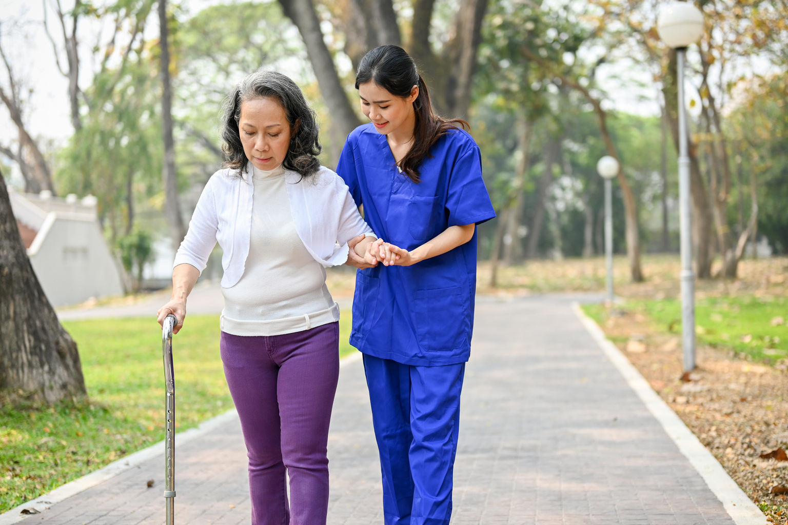 Certified nursing assistant helps patient down a walkway