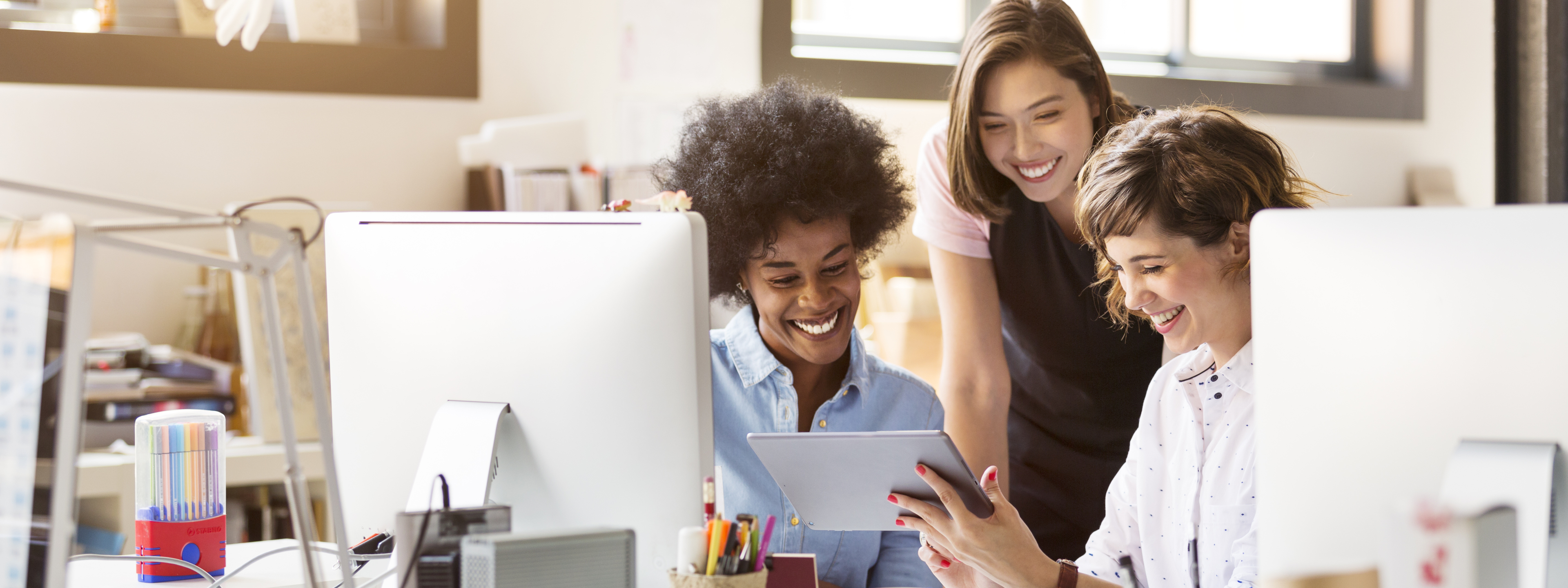 Happy multi-ethnic businesswomen using digital tablet at desk in office