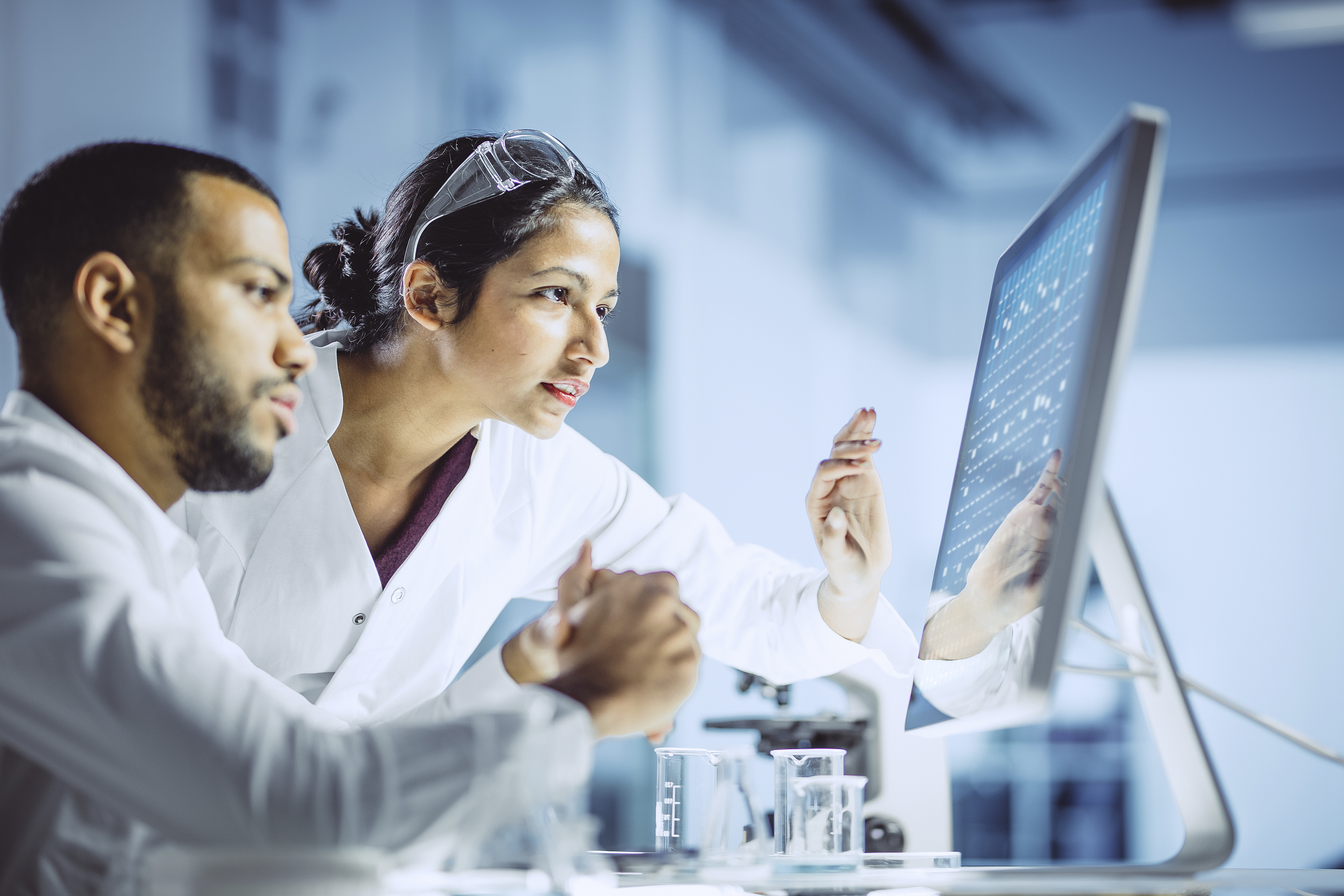 Male and female scientists looking at screen in laboratory.