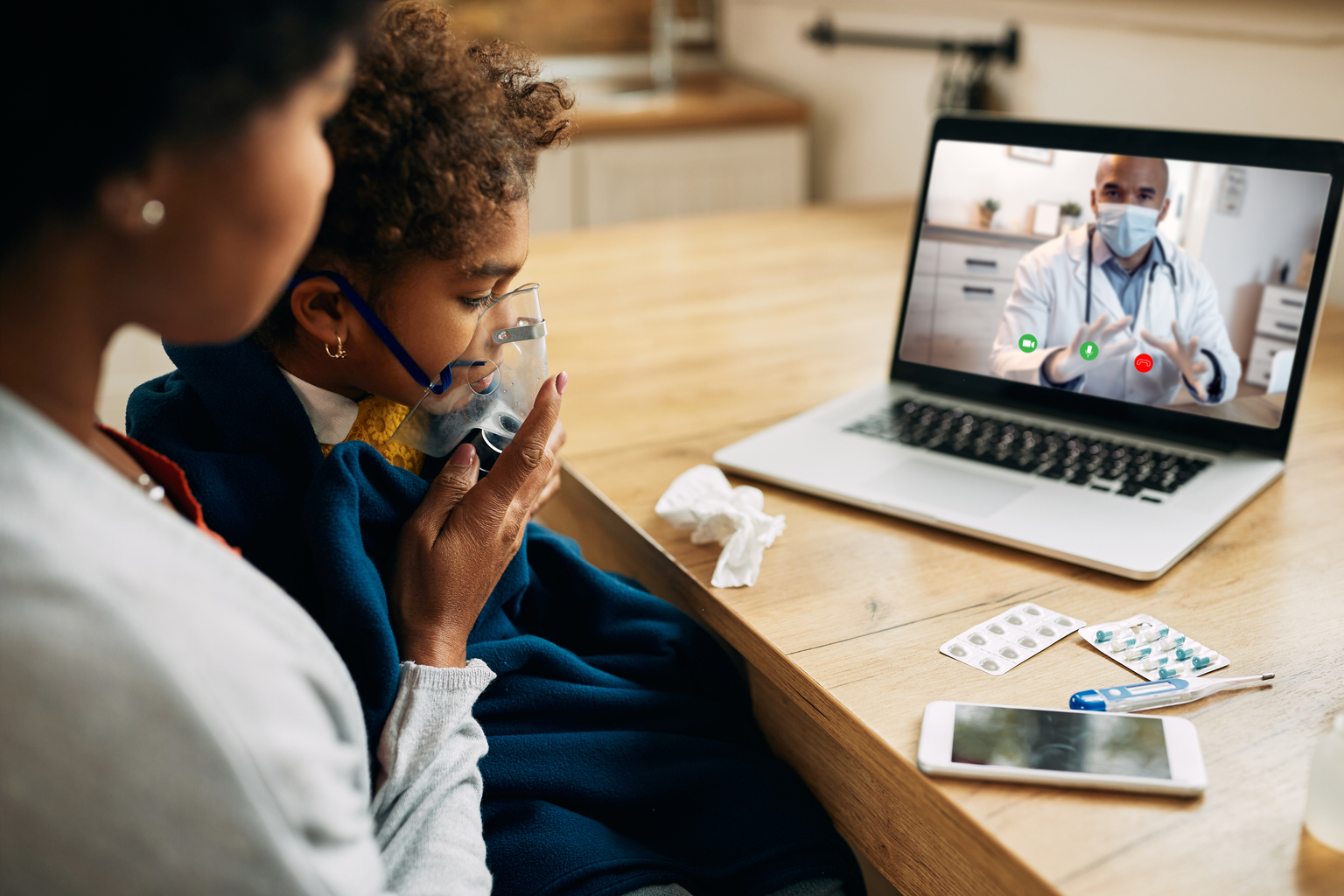 Black pediatrician talking via video call to the mother who is giving her daughter inhaling therapy at home