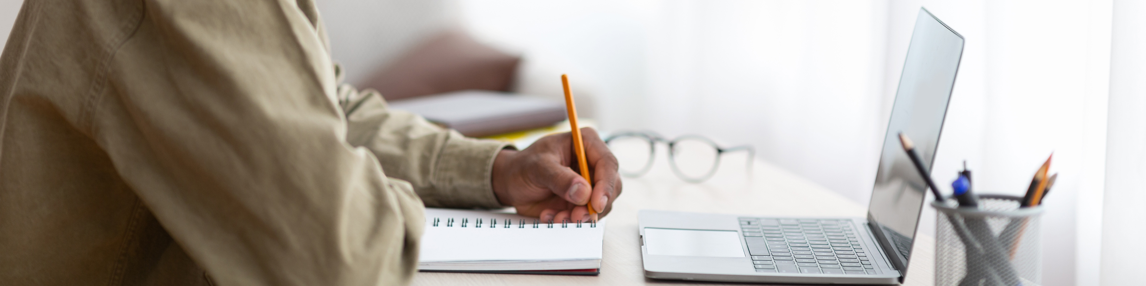 Side view of black teen taking notes in copybook during web conference at home