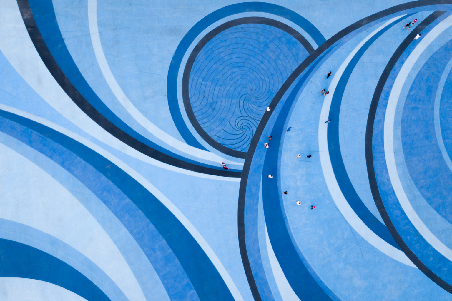 Aerial Drone View of People walking over a Circular Swirl Patterned Blue Floor,