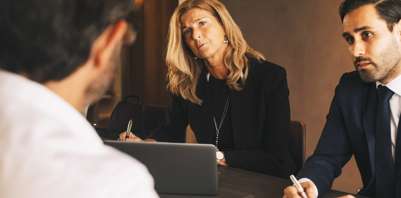 Serious legal coworkers listening to mature businessman during meeting at law office