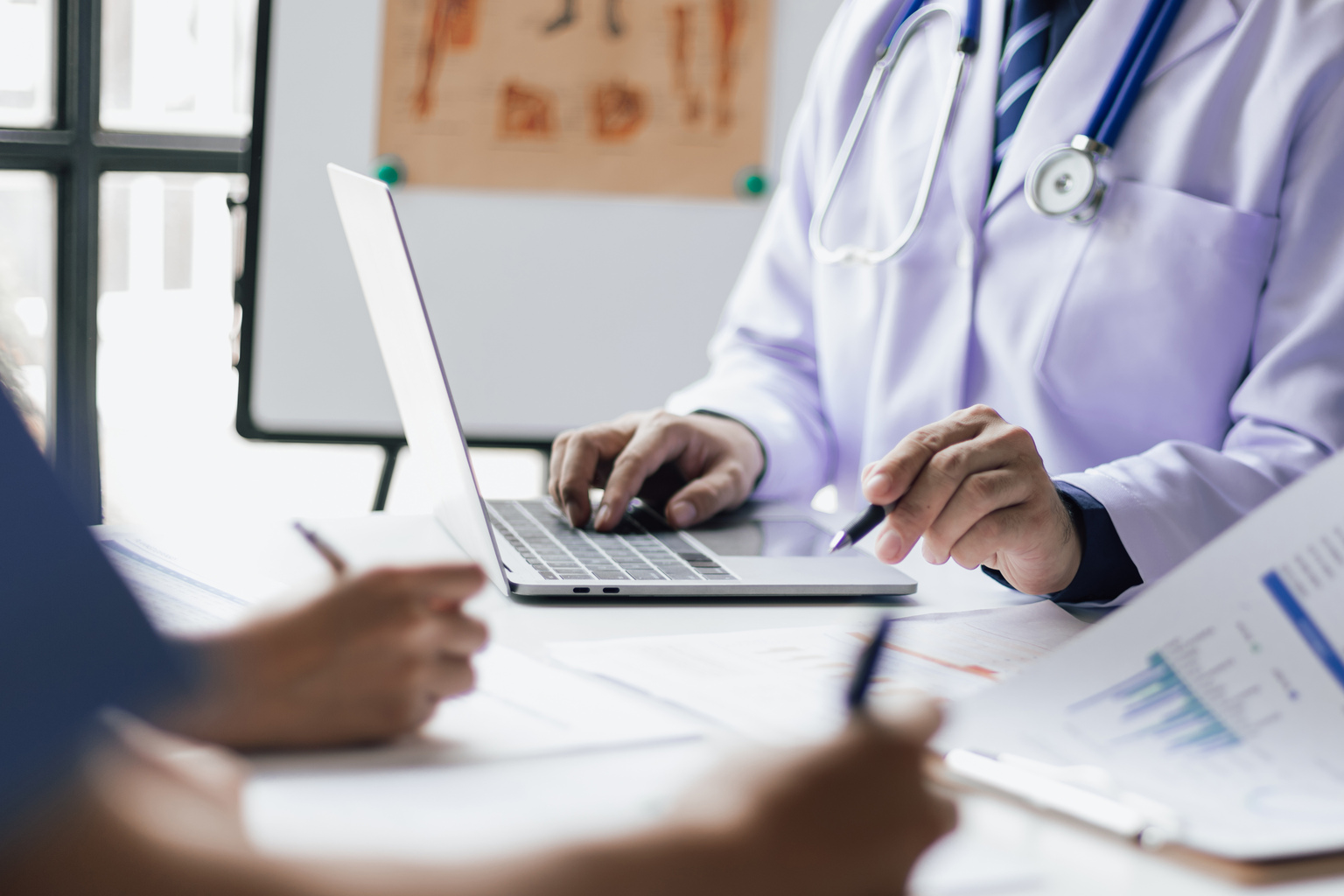 Team, medical analysts and doctors consulting with paperwork of graphs, data and charts in hospital conference room