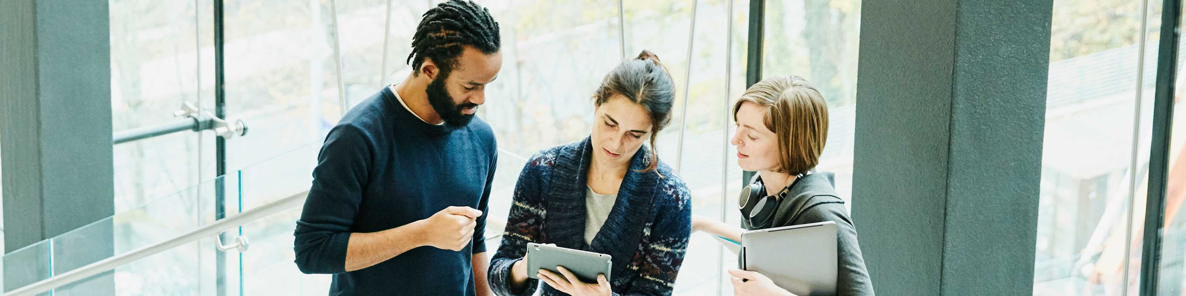 Man and two women reviewing tablet in office stairway