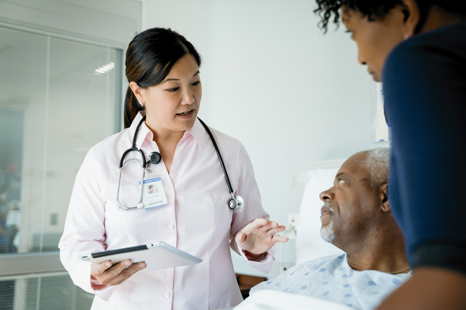 Female doctor with tablet talking to senior African patient lying by daughter.