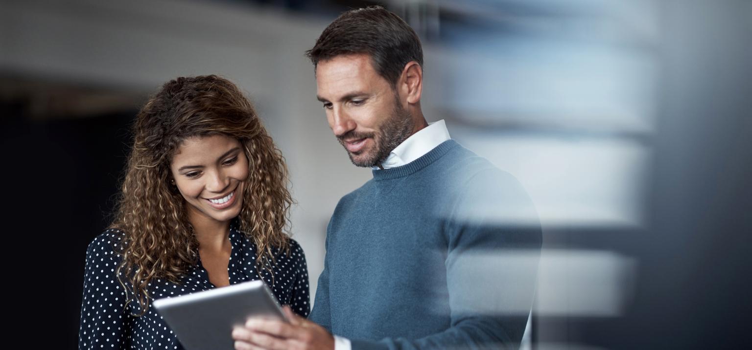 Shot of two colleagues working on a digital tablet together while standing in a large office