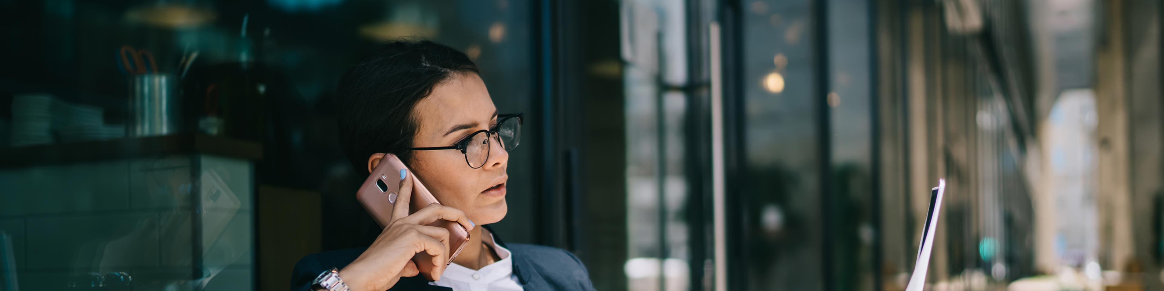 business woman sitting outdoors on the phone looking at her laptop