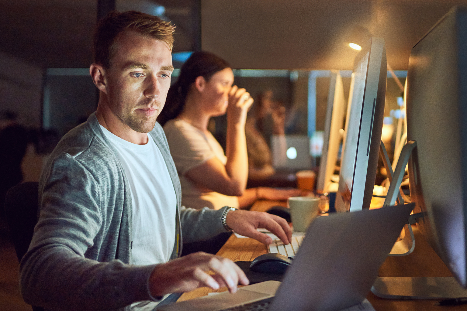 Shot of a young man using a computer and laptop during a late night in a modern office