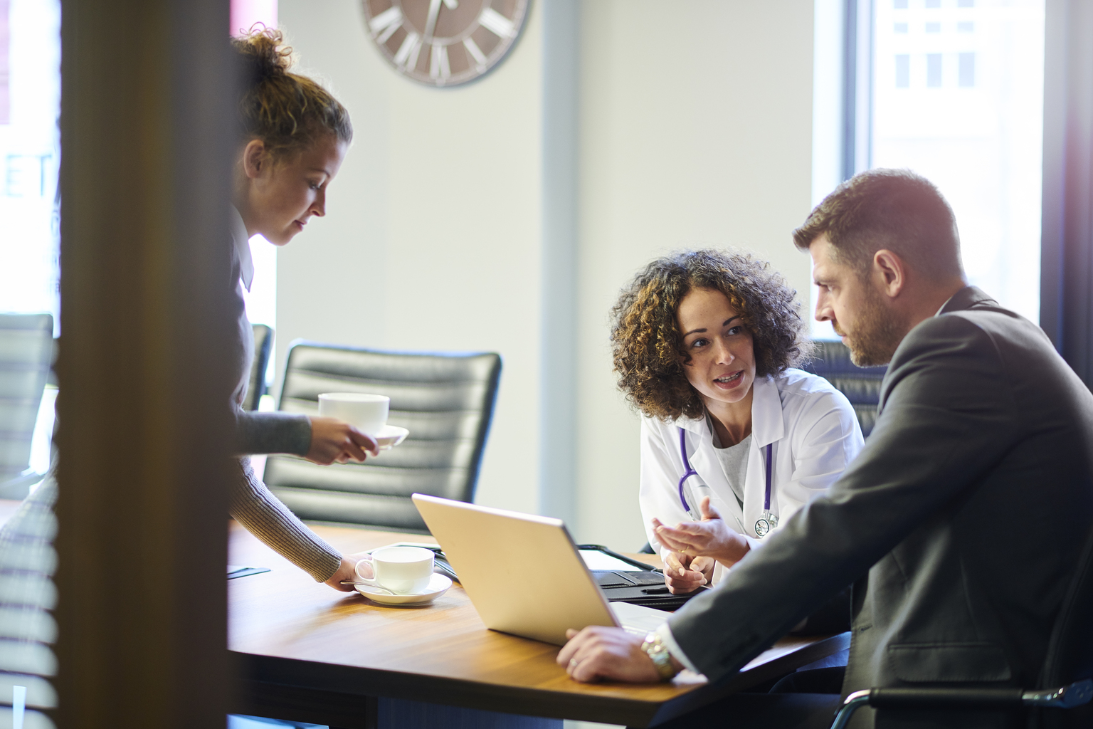 A businessman chats with a female doctor as they leave a boardroom meeting in a hospital.