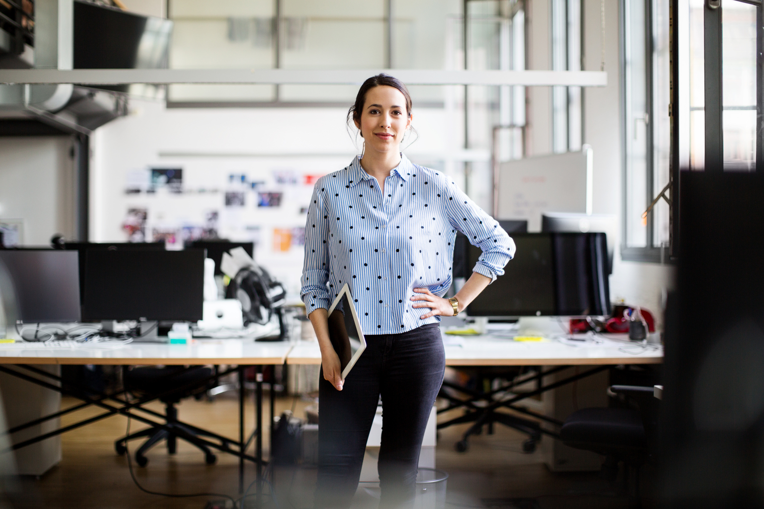 Portrait of confident female entrepreneur standing with hand on hip while holding digital tablet at creative office