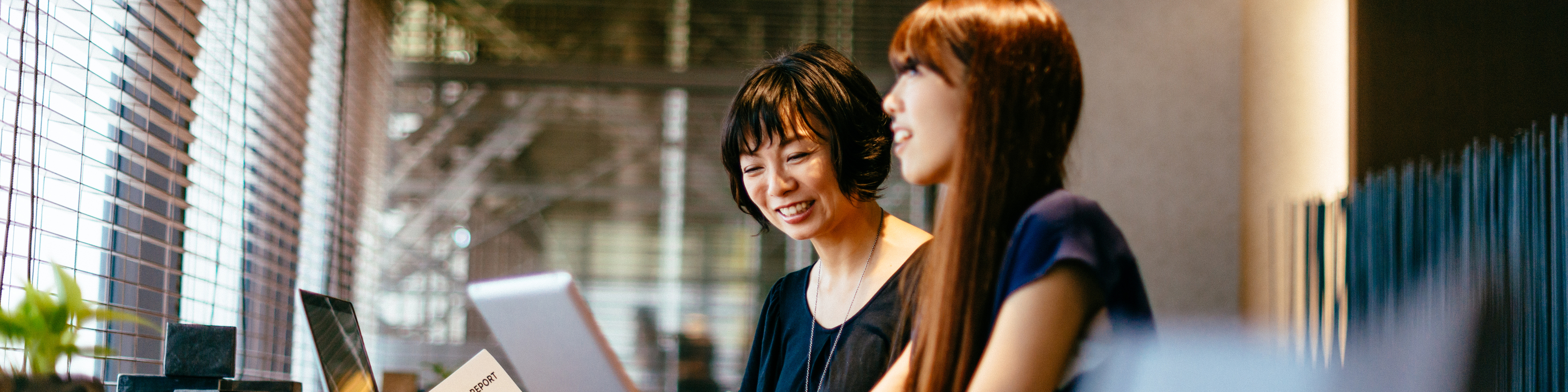 Asian female professionals reviewing financial reports on tablet and laptop.