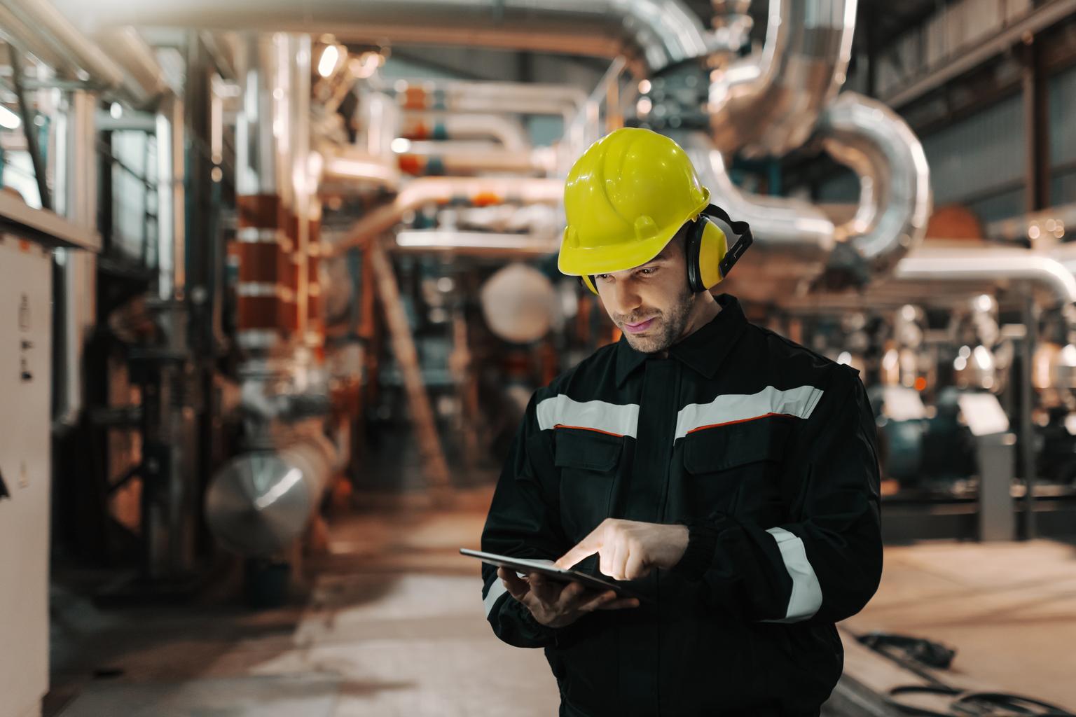 Caucasian worker in heavy industry plant with helmet and in uniform using tablet for work.