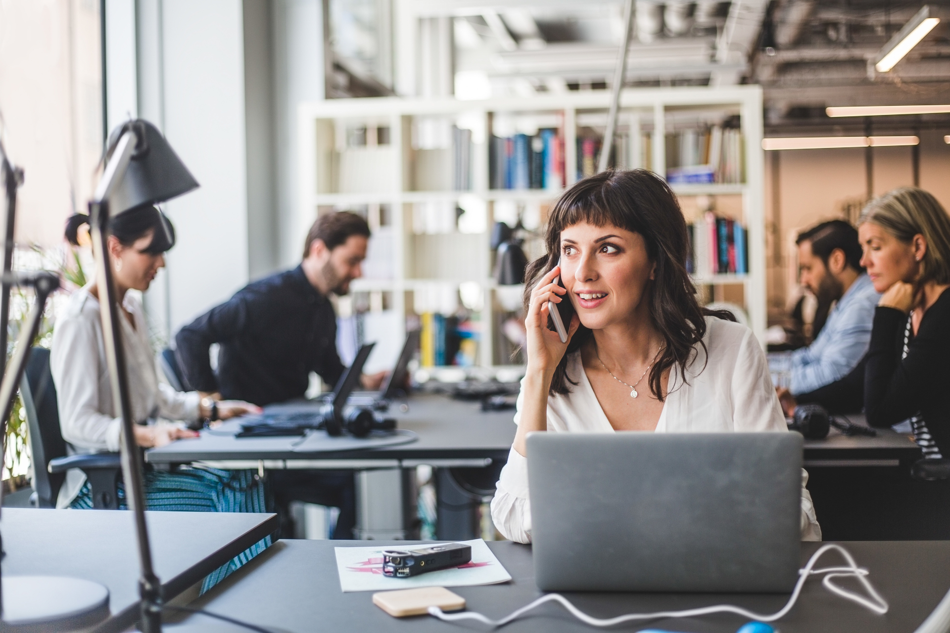 Businesswoman looking away while talking on mobile phone at desk in creative office