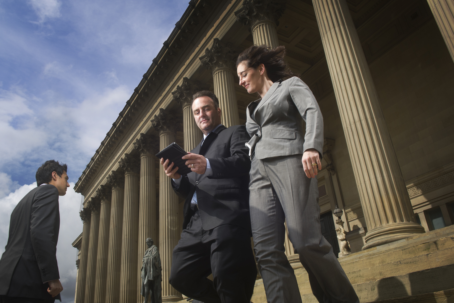 Two people in suit walking down the staircase of local government building while organizing on a tablet