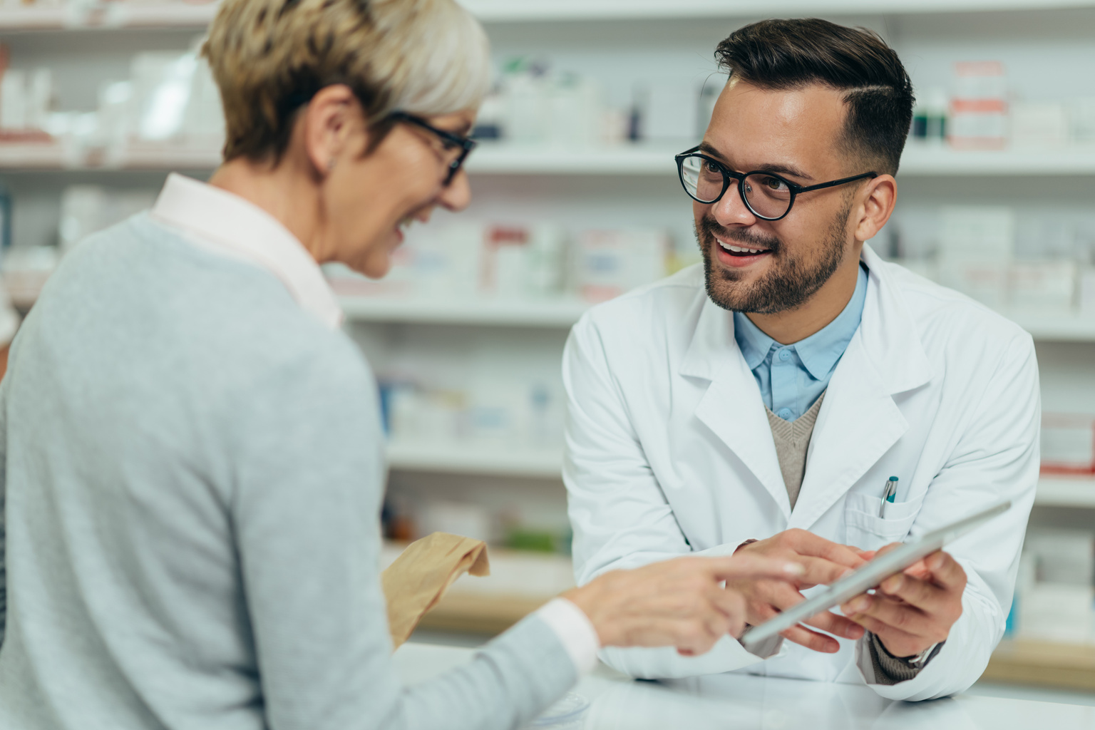 Young pharmacist with tablet advising older patient