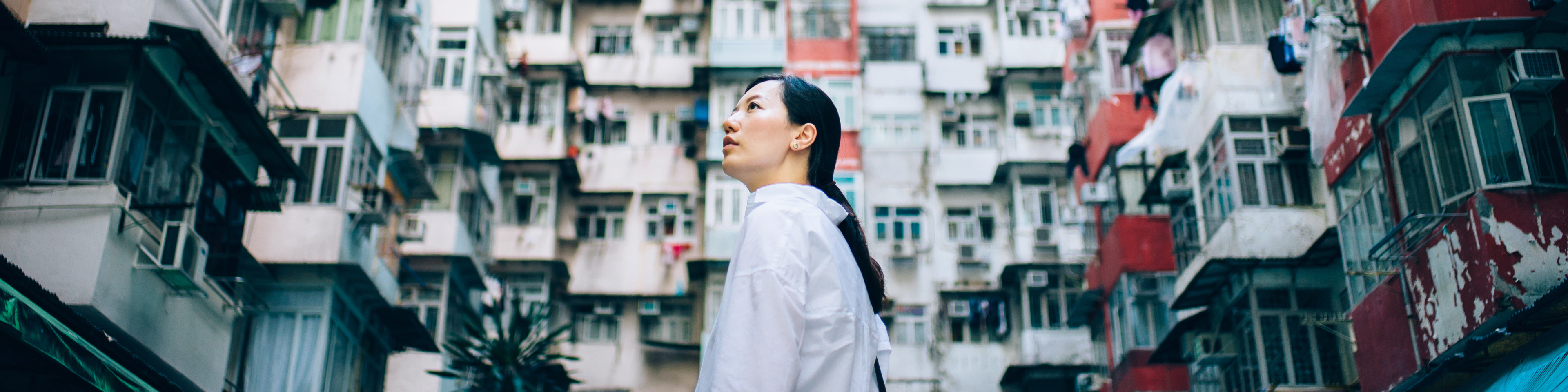 Low angle view of woman surrounded by old traditional residential buildings and looking up to sky in city