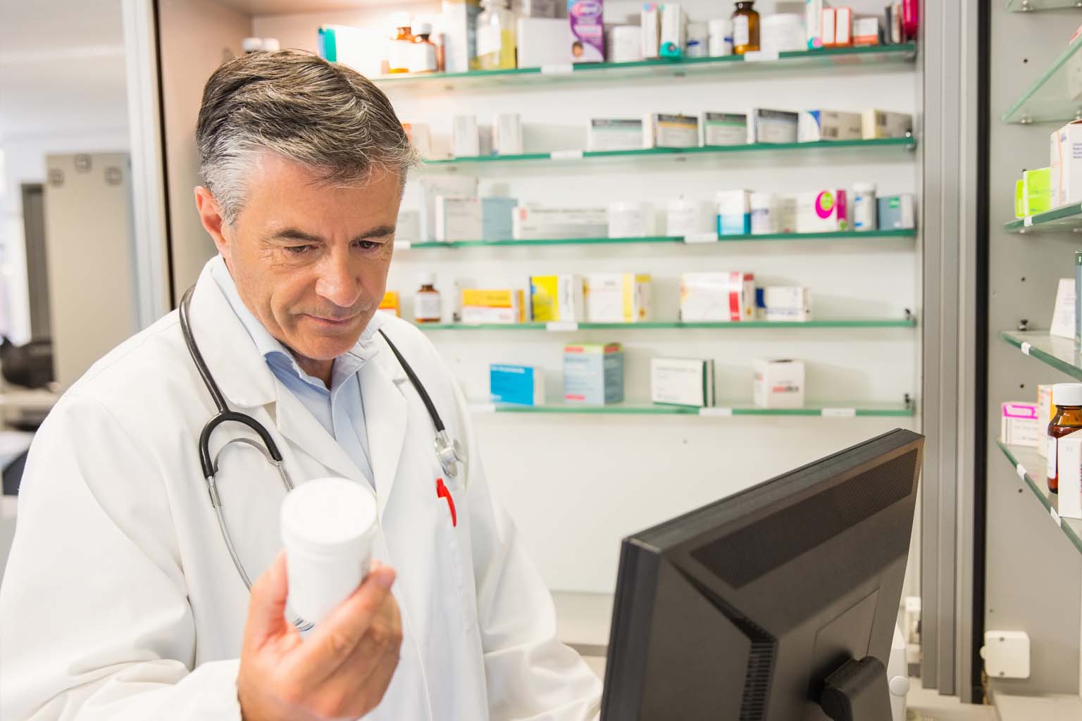 phamacist holding bottle of pills while using computer