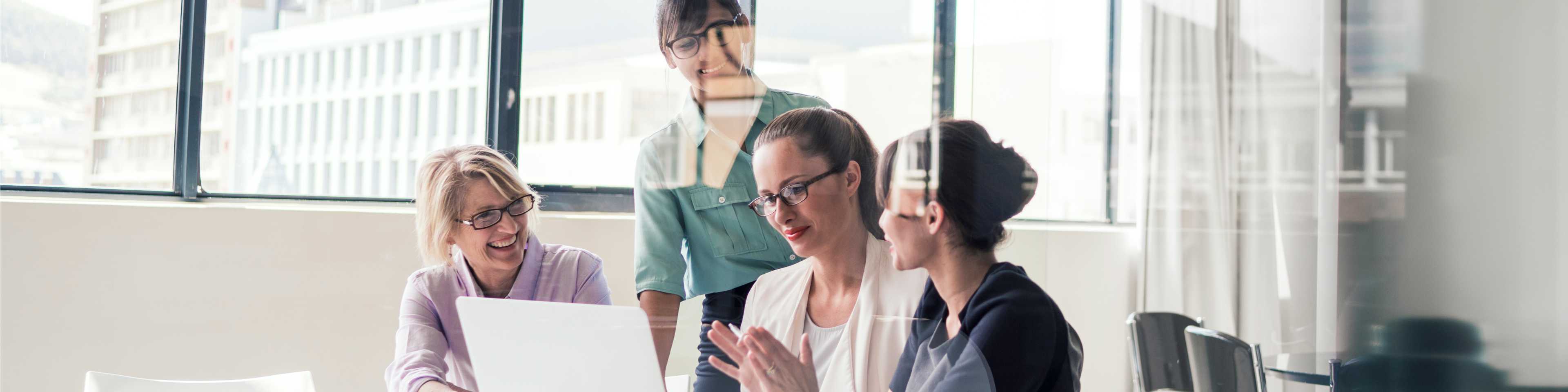 Group of women in office meeting around a laptop