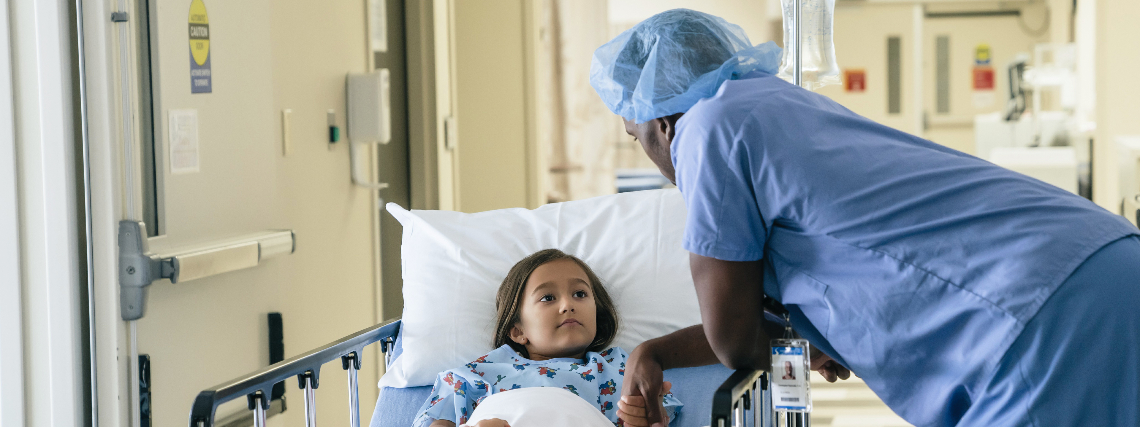 African male doctor holding hand of girl in hospital gurney.