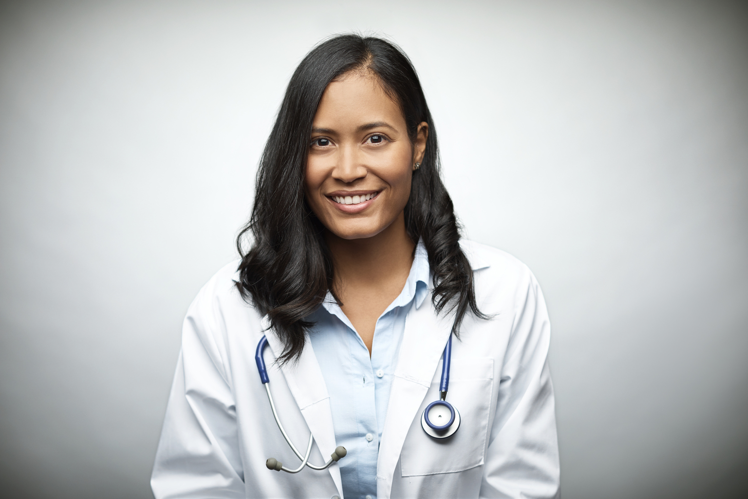 Portrait of female doctor smiling over white background. Confident healthcare worker is wearing lab coat in studio. Professional is with stethoscope.