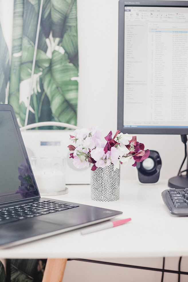 Computer desk with monitor, laptop, and small metal vase of flowers