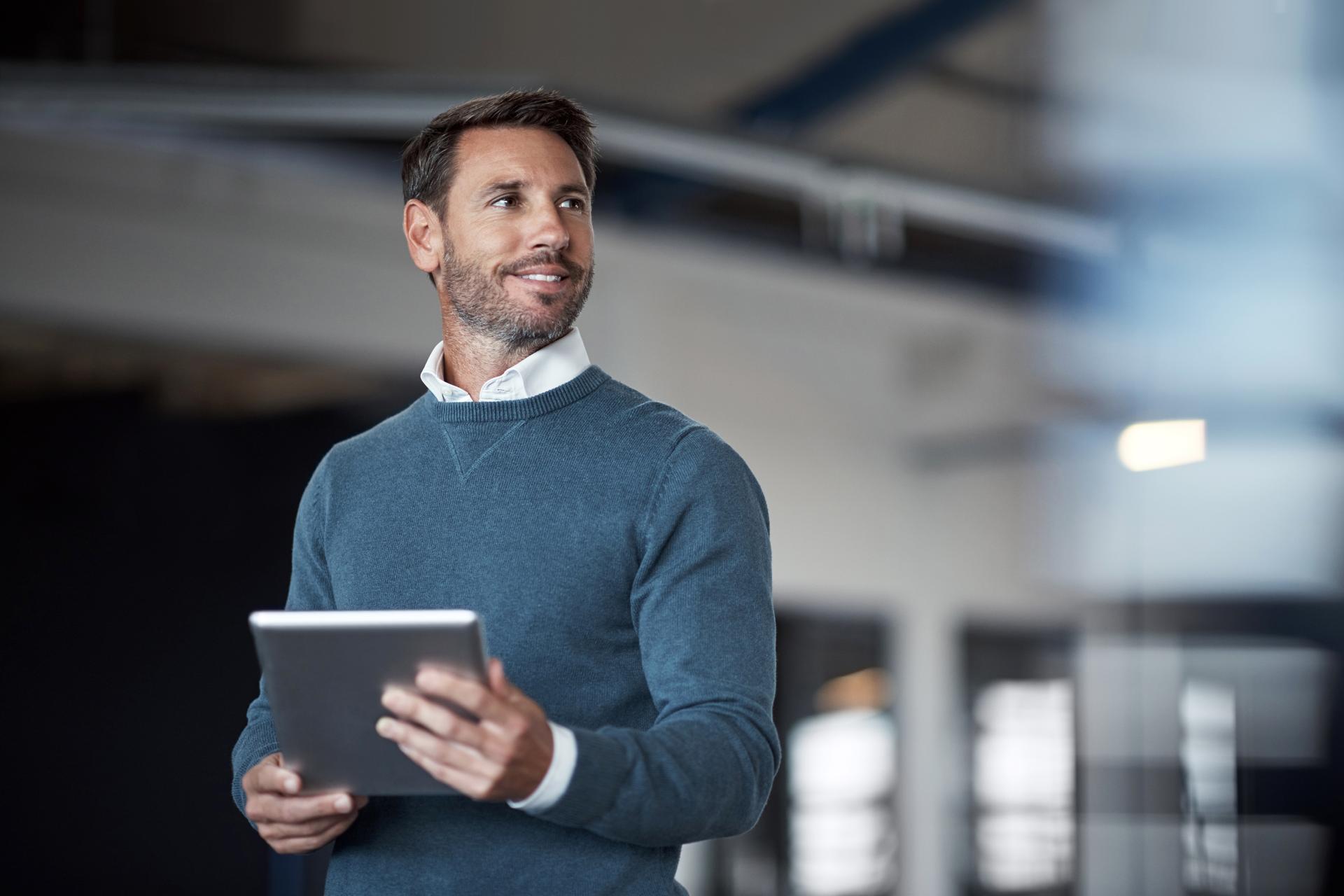 Business Mann steht und schaut aus dem Fenster, und hält dabei ein Tablet in der Hand