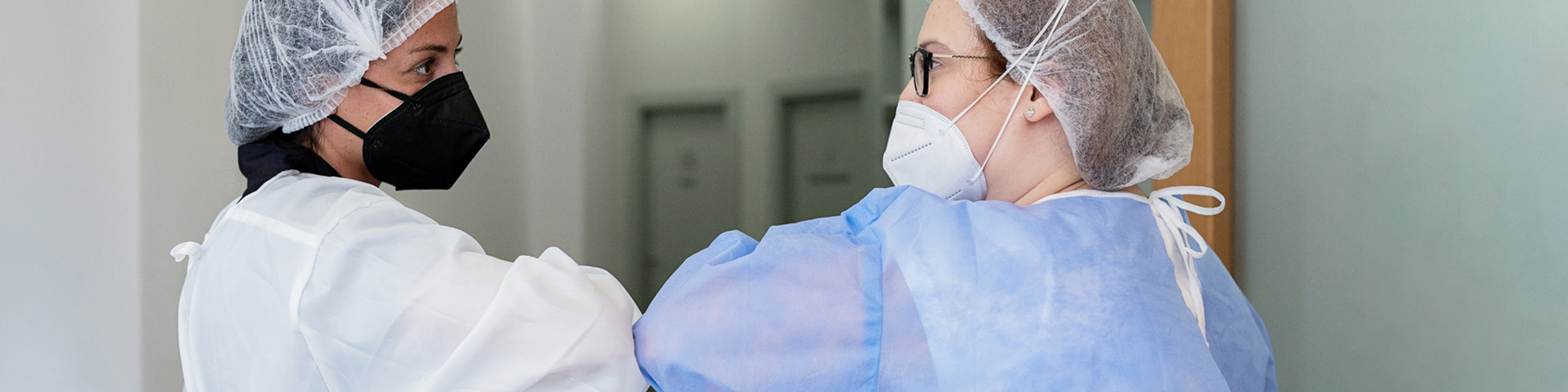 Medical workers in uniform and ppe, greeting each other with elbow bump