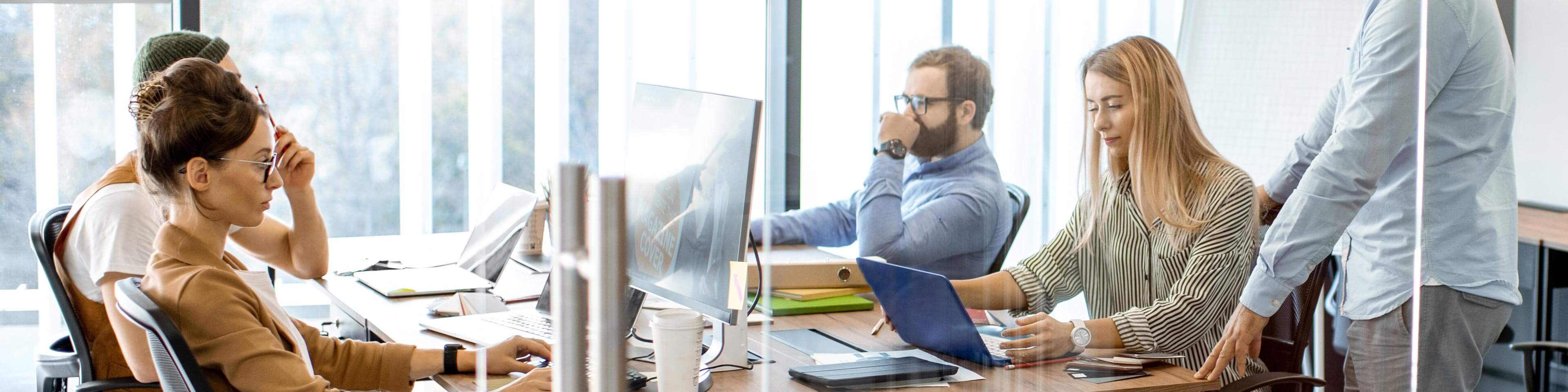 men and women in business casual attire sitting at a collaborative desk working